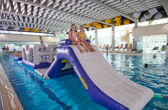 Bild aus der Vogelperspektive aufgenommen. Schwimmbecken in dem sich ein Wasserparcourpark aufgebaut ist. Kinder Klettern auf dem Parcour.