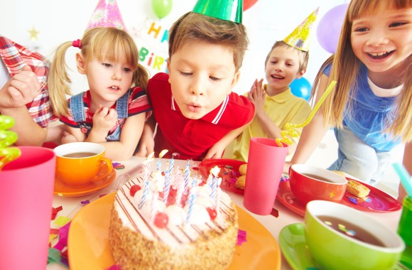 Kinder feiern und Junge bläst Geburtstagskerzen aus