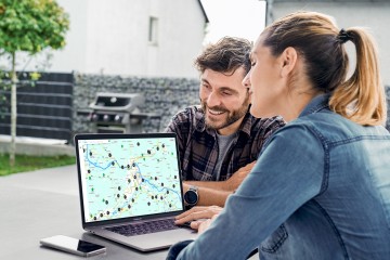 Ein Paar sitzt im Garten vor dem Laptop.