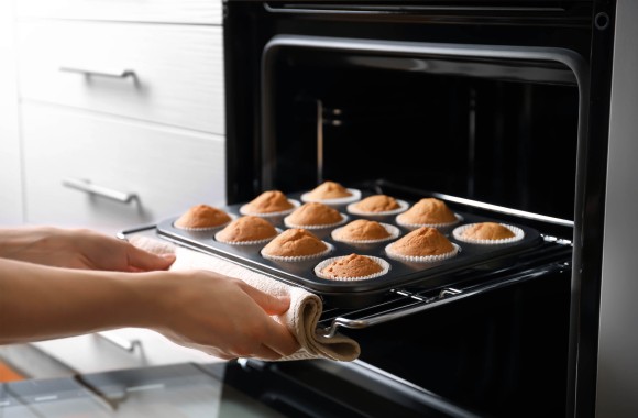 Frau, die ein Blech mit Muffins aus dem Ofen nimmt