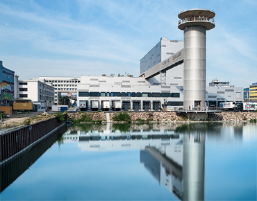 Ansicht auf den Turm neben dem Hafenbecken mit dem Hafenpark im Hintergrund.