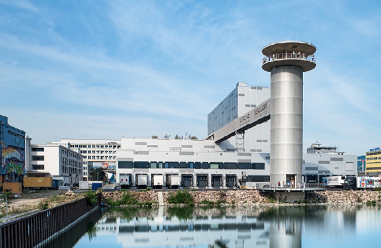 Ansicht auf den Turm neben dem Hafenbecken mit dem Hafenpark im Hintergrund.