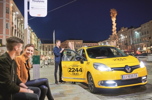 Zwei junge Menschen steigen in ein gelbes Linzer Taxi am Hauptplatz ein.