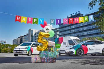 3 Fahrzeuge von tim vor der Linz AG-Zentrale, im Vordergrund Luftballons und Geschenkspäckchen, ein Luftballon hat die Form "5"