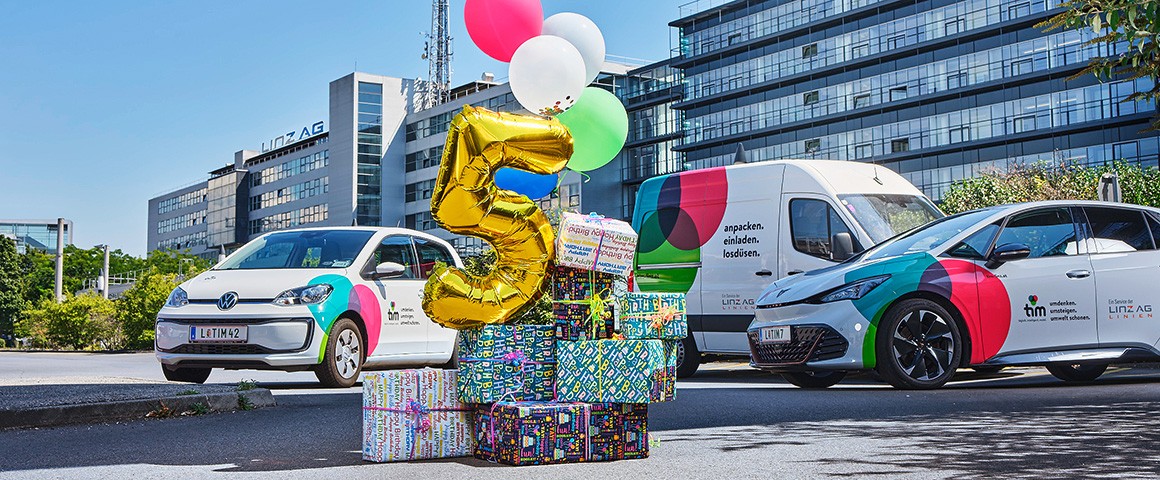 3 Fahrzeuge von tim vor der Linz AG-Zentrale, im Vordergrund Luftballons und Geschenkspäckchen, ein Luftballon hat die Form "5"