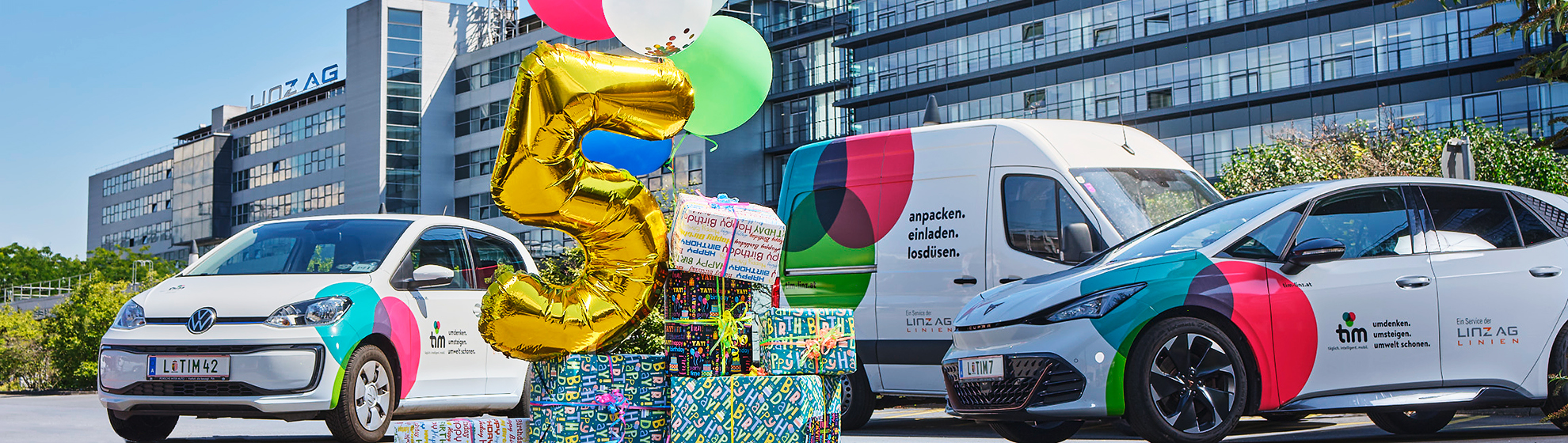 3 Fahrzeuge von tim vor der Linz AG-Zentrale, im Vordergrund Luftballons und Geschenkspäckchen, ein Luftballon hat die Form "5"