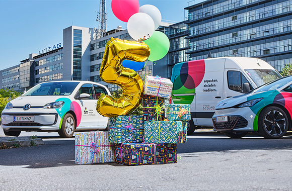 3 Fahrzeuge von tim vor der Linz AG-Zentrale, im Vordergrund Luftballons und Geschenkspäckchen, ein Luftballon hat die Form "5"