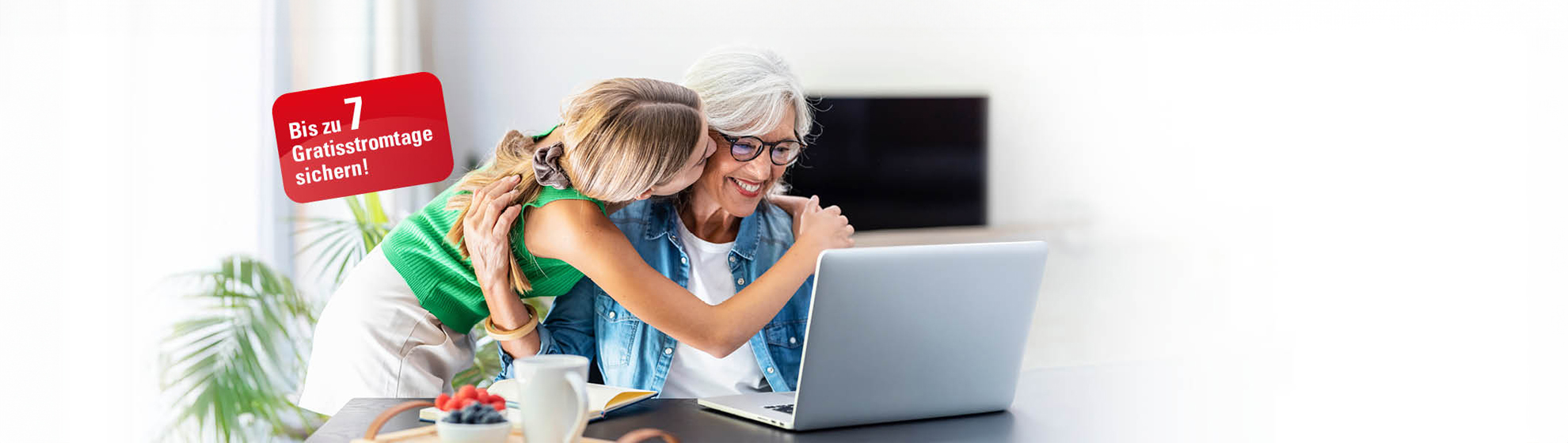 Eine ältere Frau sitzt vor dem  Laptop, während ihre Enkelin sie umarmt und küsst. Neben den Personen ist die Botschaft "Bis zu 7 Gratisstromtage sichern!" zu sehen.