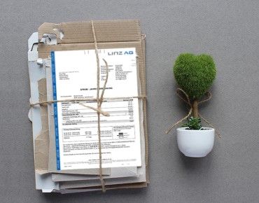 Abbildung eines Stapels Altpapier mit einer LINZ AG-Rechnung und ein grünes Bäumchen in einem Topf