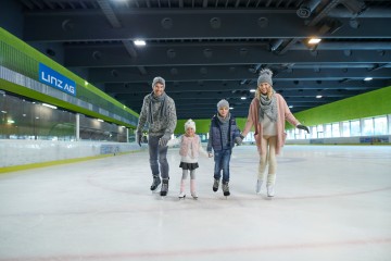 Frau und Mann mit zwei Kindern Hand in Hand auf dem Eis in der Eishalle Parkbad