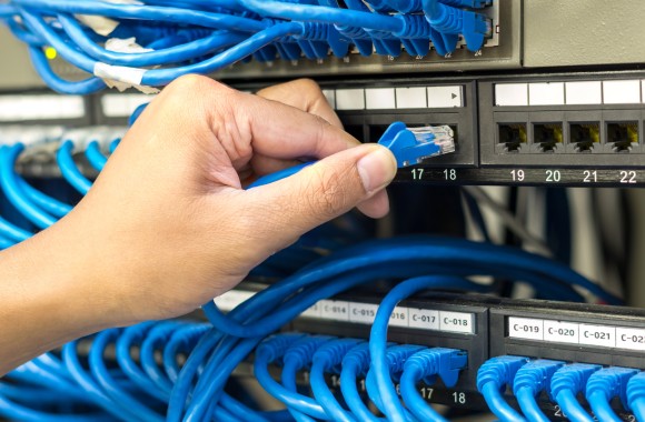 Eine Hand steckt in einem Serverschrank eine Kabel aus einem Server Rack