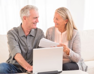 Älteres Paar sitzt mit Dokumenten vor dem Computer