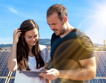 Eine Frau und ein Mann stehen vor einer Photovoltaikanlage und schauen gemeinsam in ein Tablet.