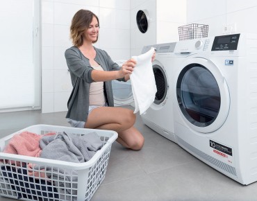 Eine Frau kniet vor der Waschmaschine und legt die Wäsche von der Waschmaschinentrommel in den Wäschekorb, der neben ihr steht.