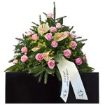 grünes Bukett mit rosa Rosen und grün-rosa Calla mit weißer Schleife steht auf schwarzem Podest