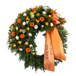 grüner Kranz dekoriert mit gelben Rosen, orangenen Gerbera und weißen Nelken, dazu eine orangene Schleife mit Aufschrift "in ewig Mein, in ewig Dein"