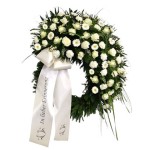 grüner Kranz mit vielen weißen Blumen und weißer Schleife mit Aufschrift "in lieber Erinnerung"