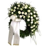 grüner Kranz mit vielen weißen Blumen und weißer Schleife und Goldabschluss mit Aufschrift "in lieber Erinnerung"