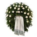 grüner Kranz mit weißen Gerbera und weißen Rosen, dazu eine weiße Schleife mit Aufschrift "in lieber Erinnerung"