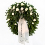 grüner Kranz mit weißen Rosen, Nelken und Schleierkraut. Dazu eine weiße Schleife mit Aufschrift "in lieber Erinnerung"