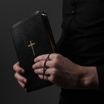 Foto von Händen, welche ein schwarzes Buch und ein Kreuz halten